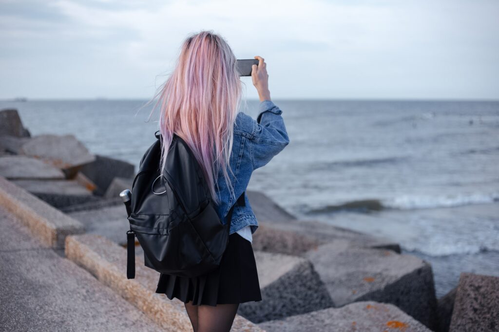 A young person with colorful hair taking a selfie at the beach