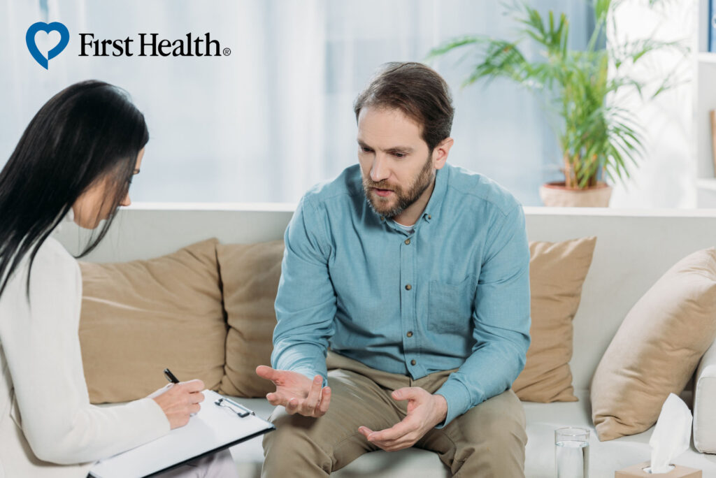 man discussing his addiction problems with therapist at a rehab that accepts First Health rehab coverage